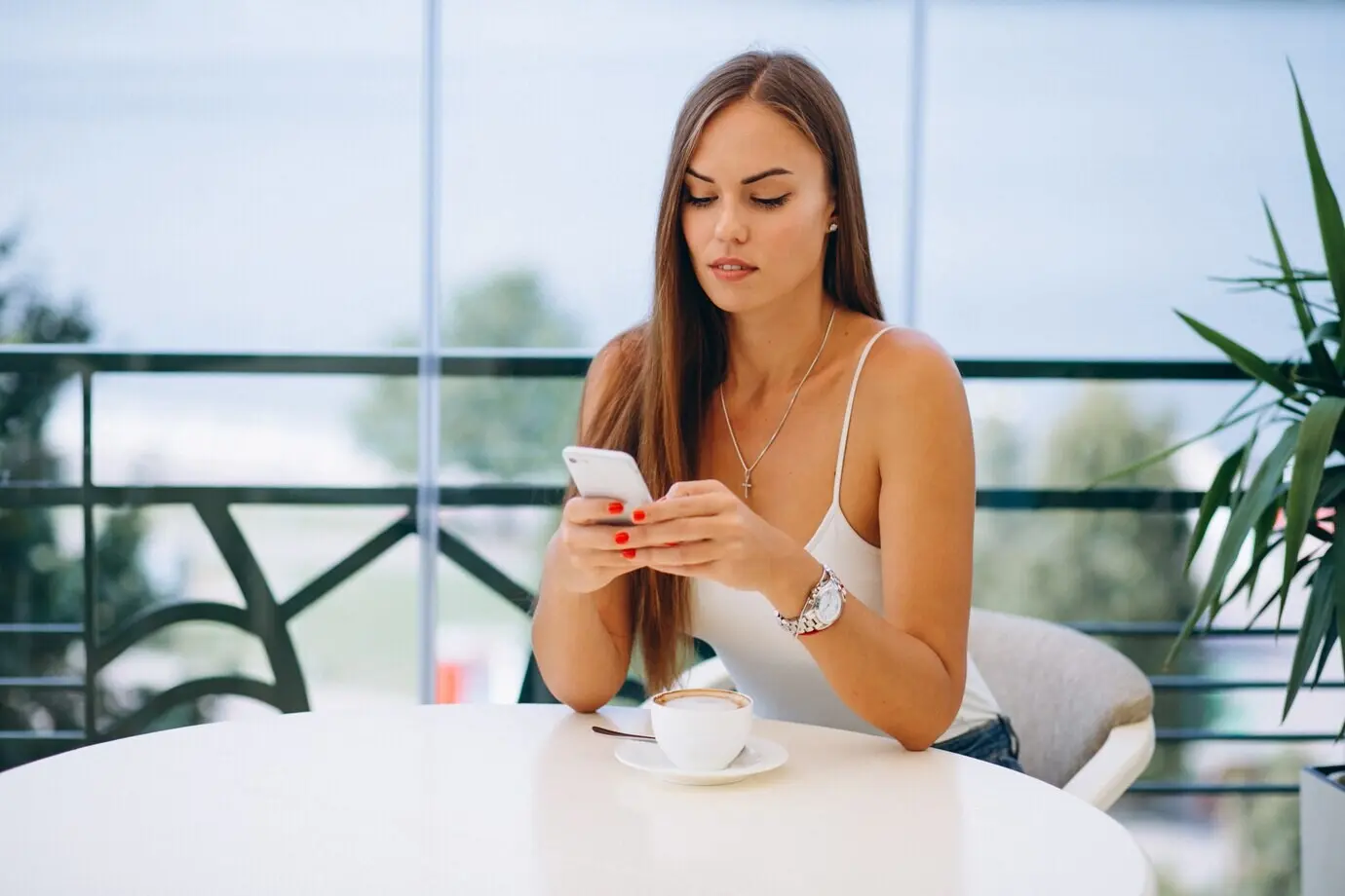 A woman at a café, drinking tea while using a phone.