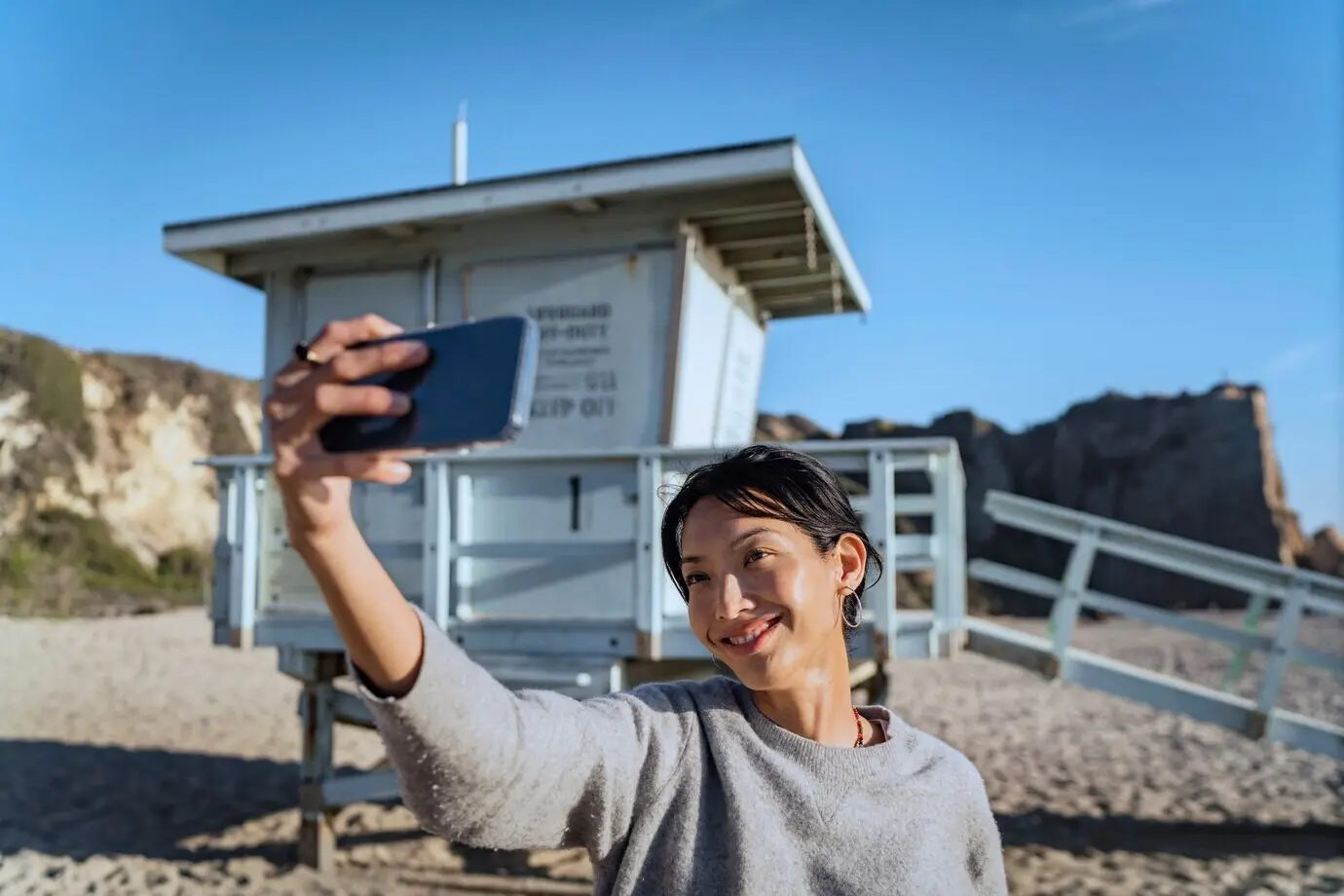 A young woman uses her smartphone to take a selfie at the beach.