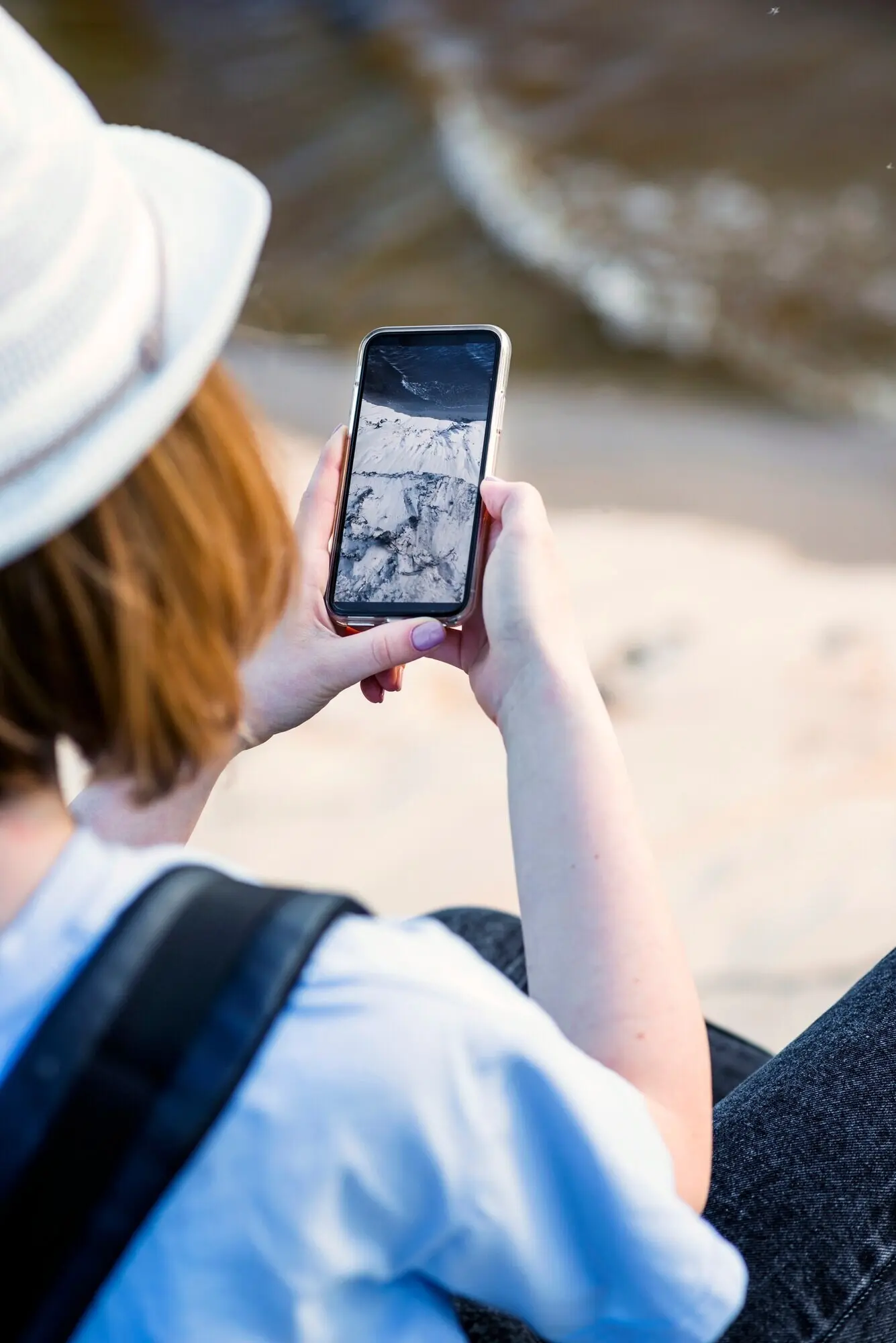 Cropped image of a woman taking a photo of the sea and sand.