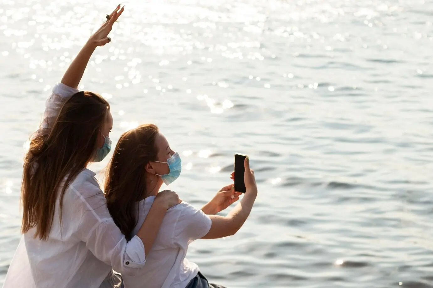 Side view of female friends wearing face masks taking a selfie by the lake